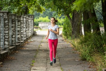 Young woman running on the track through the summer park.