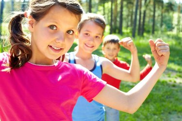 Three young children pose outdoors, flexing their biceps.