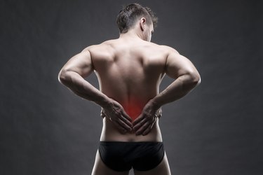 Kidney pain. Man with backache. Handsome muscular bodybuilder posing on gray background with red dot