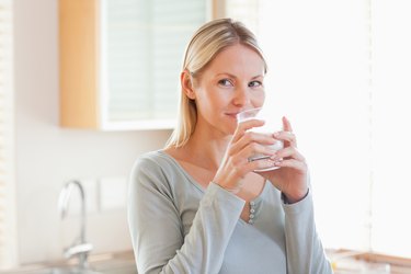 Woman standing in the kitchen drinking some water