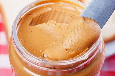 A knife scoops peanut butter out of a jar.