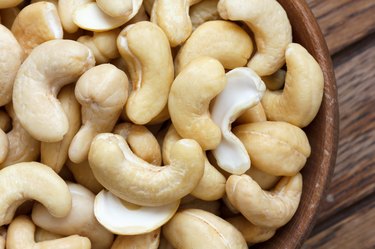 Wooden bowl of cashew nuts from above. On dark wood.