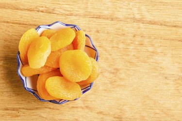 Bowl of dried apricots on wooden table background.