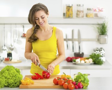 happy young woman cutting fresh vegetables in kitchen