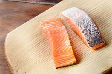 Two raw salmon fillets on wooden cutting board won't cause vitamin D3 stomach upset