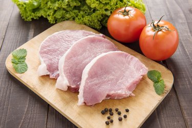 Raw pork on cutting board and vegetables.