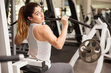 Rear view portrait of a gorgeous strong woman exercising her muscles at the gym and making eye contact