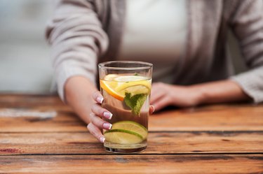 A woman drinking a glass of water with lemon and lime slices