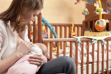 Mother breastfeeding her baby in front of a crib