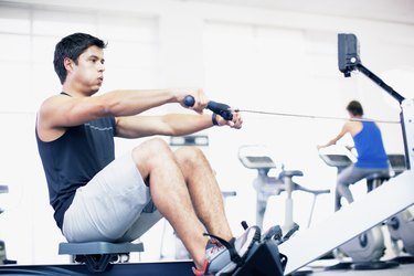 Young man exercising on rowing machine in gymnasium