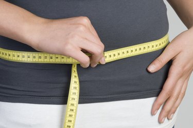 close up of a person's midsection with a yellow measuring tape wrapped around it to measure the hips