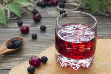close up of glass of tart cherry juice on a wooden table, with berries on the table