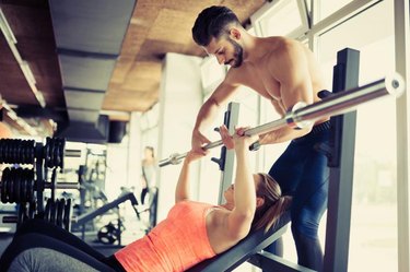 A personal trainer assists a woman with her bench press at the gym.