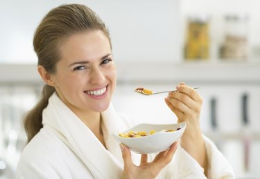 happy young woman eating muesli in kitchen