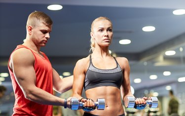 young couple with dumbbells flexing muscles in gym