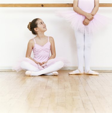 Seated Young Ballet Dancer Looking Up at Another Ballet Dancer Standing in a Dance Studio
