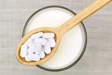 Wooden spoon of Calcium carbonate tablets above glass of milk