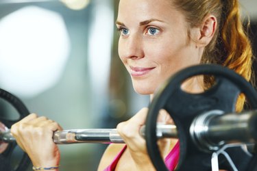 Young woman exercising with barbell in gym.