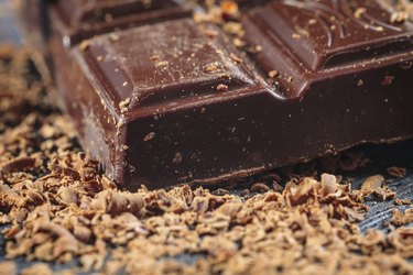 A bar of dark chocolate and chocolate shavings on a cutting board.