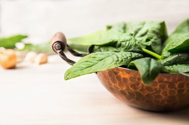 Fresh spinach leaves in copper pan on white wooden background