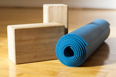 A blue yoga mat with two wooden yoga blocks sit on a wooden yoga studio floor before class.