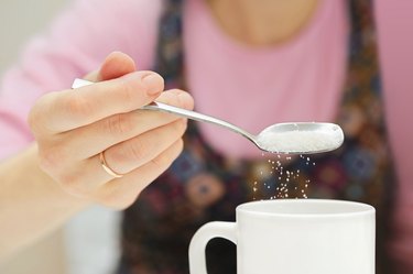 woman holds a spoon and strews sugar to mug