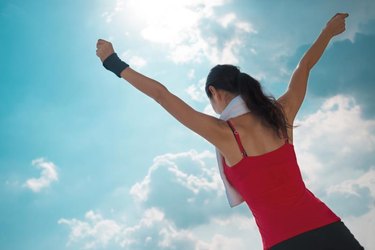 Active woman with outstretched arms against the blue sky, rear view