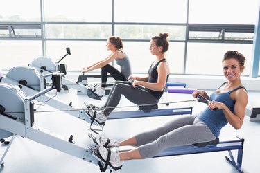 Happy woman using rowing machine with friends