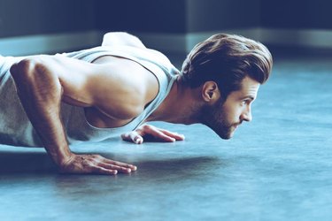 Side view of young handsome man in sportswear doing push-up at gym