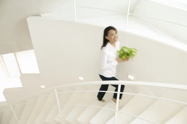 Blurred Motion Shot of a Woman Ascending a White Stairway Carrying a Potted Plant