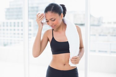 Tired dark haired model in sportswear drying herself with a towel