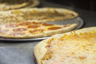 A thin crust cheese pizza with others waiting to be served.