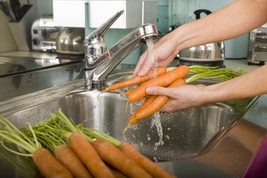 Woman washing carrots at kitchen sink, close-up