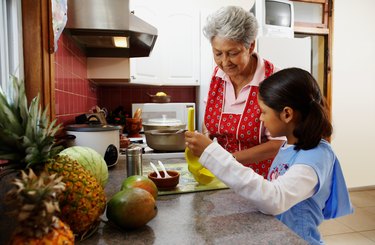 Girl (6-8) assisting grandmother in kitchen, side view