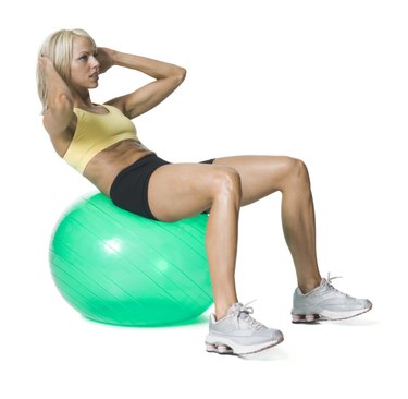 full body shot of a young woman in a yellow and black exercise outfit as she does sit ups on a green ball