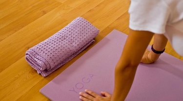 women hands on a ''YOGA'' printed yoga mat,on a wooden floor with towel