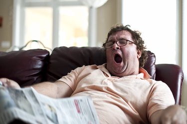 Adult male yawning while on the couch reading a newspaper