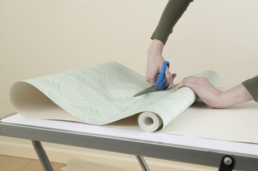 Person cutting through roll of wallpaper