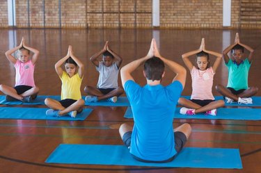 School kids and teacher meditating during yoga class in basketball court at school gym