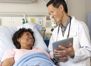 Doctor Using Digital Tablet Talking With Senior Patient