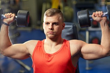 young man with dumbbells flexing muscles in gym