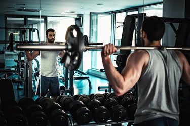 Man watching himself in the mirror while doing squats in the gym