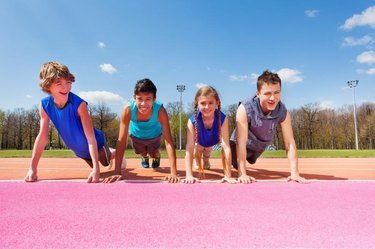 Four happy smiling teenagers doing push-up exercises standing in a row outdoor on the track