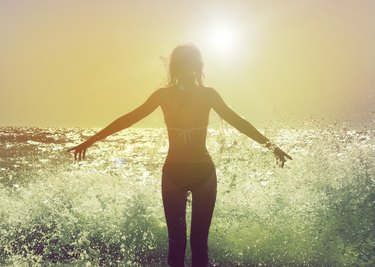 Woman facing the sun with waves crashing at her feet