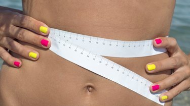 Girl measuring her waist at the seaside