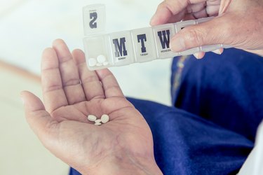 old woman hand pouring pills from a pill reminder box