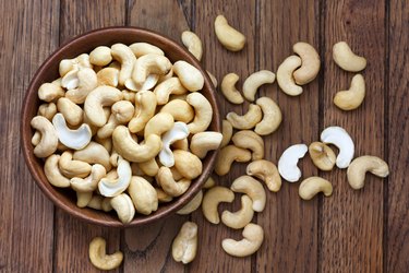 Wooden bowl of cashew nuts from above. On dark wood.