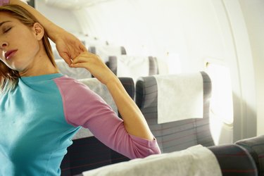 Woman in airplane with hands behind head, eyes closed