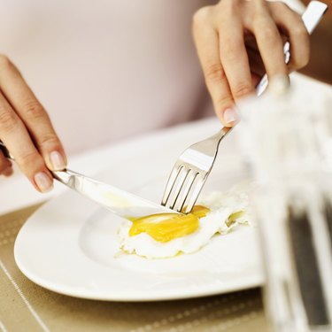 Close-up of a woman's hands cutting a fried egg with a fork and knife