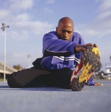 Male athlete stretching on track in stadium, ground view